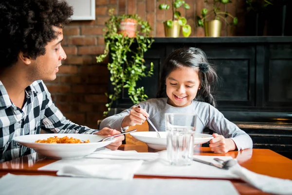 Latin dad and daughter eating together lunch at restaurant, multiethnic family having fun