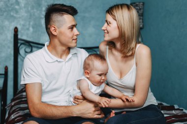 Kollarını birbirine bakarak sevgiyle cradling bebek kızı yatağa evde oturan anne sevgi dolu. Çocukluk, ebeveynlik, beraberlik, aşk, mutluluk kavramı