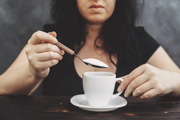 woman pouring sugar into coffee cup