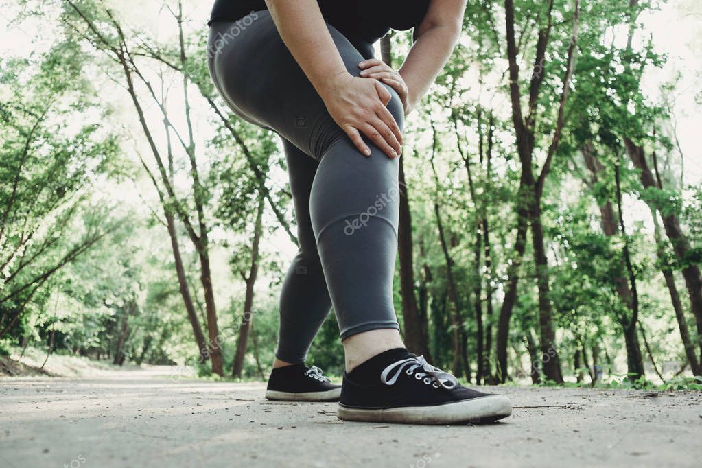 Fat woman holding injured leg at outdoor jogging