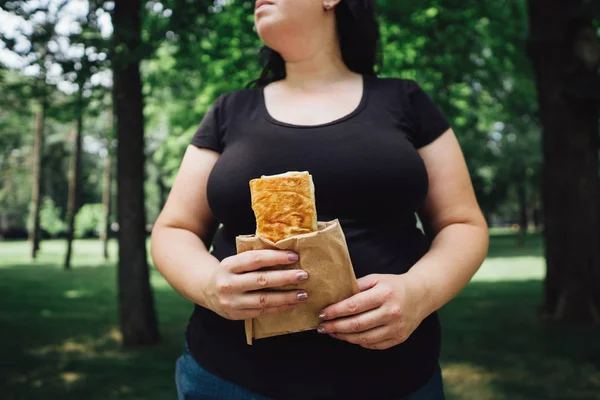 Надмірна вага жінка їсть донорський шашлик, що йде на відкритому повітрі — стокове фото