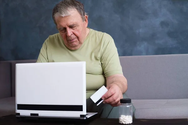Старший мужчина с кредитной картой оплачивает счета на ноутбуке — стоковое фото