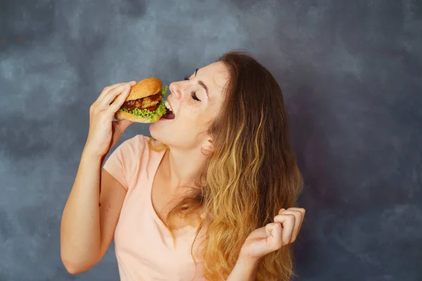 Mujer joven comiendo hamburguesa apetitosa codiciosamente —  Fotos de Stock