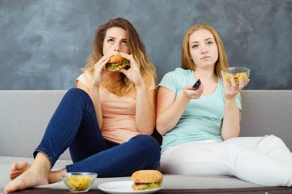 Mulheres jovens com tv remoto comer fast food — Fotografia de Stock