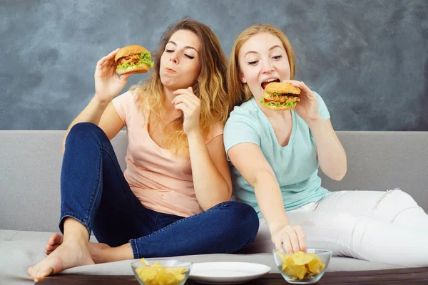 Дві молоді жінки з жадібністю їдять бургерів і чіпсів — стокове фото