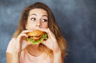 Young woman eating greedily big tasty hamburger clipart