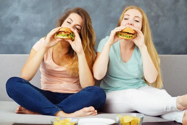 Duas jovens comendo hambúrgueres e batatas fritas — Fotografia de Stock