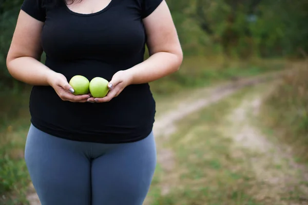 Overweight woman with two green apples in hands