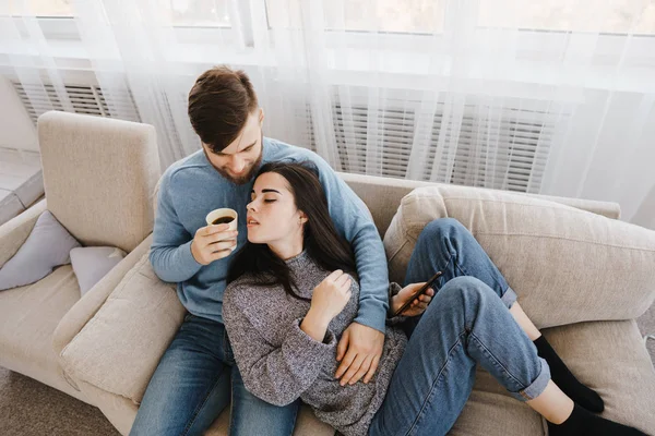 Νεαρό ζευγάρι κάθεται στο καναπέ με ζεστά ροφήματα — Φωτογραφία Αρχείου