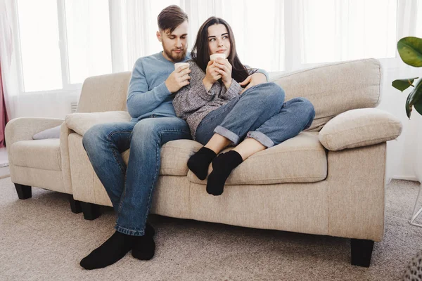A fiatal pár ül a kanapén, forró italok — Stock Fotó