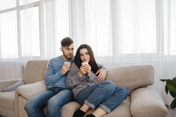 A fiatal pár ül a kanapén, forró italok — Stock Fotó
