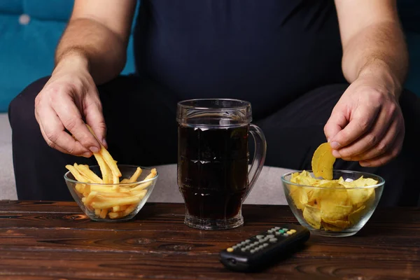 Hombre con sobrepeso con control remoto de televisión, comida chatarra y cerveza — Foto de Stock