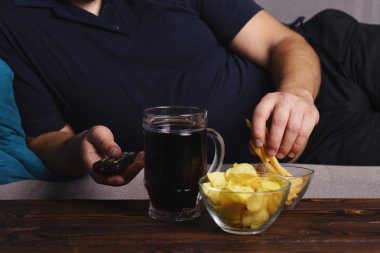 overweight man with tv remote, junk food and beer clipart