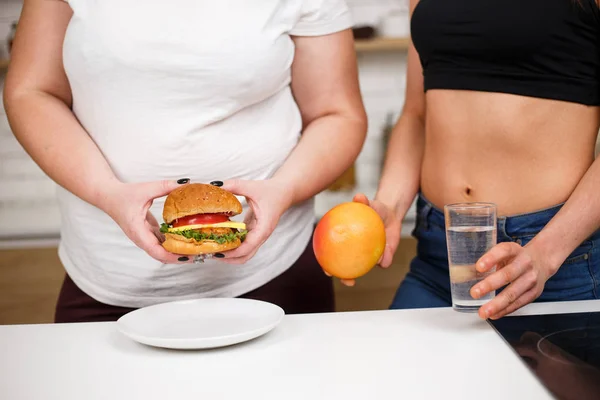 Mulher obesa com hambúrguer e nutricionista com frutas — Fotografia de Stock