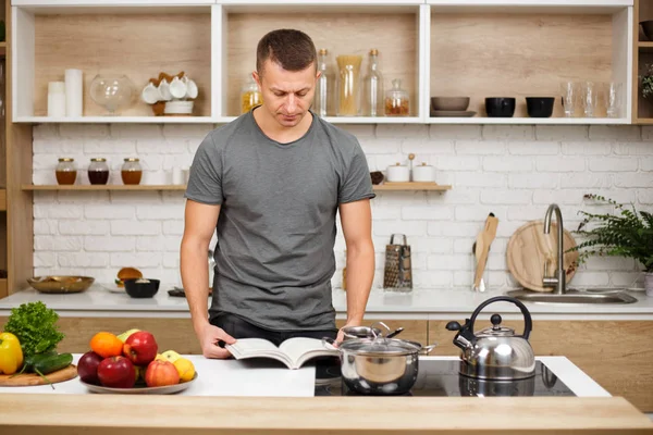 Ajuste homem musculado leitura livro de receitas antes de cozinhar — Fotografia de Stock