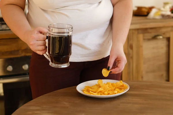 Mujer con sobrepeso merienda con cerveza y patatas fritas — Foto de Stock