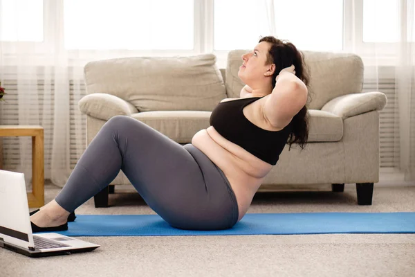 Överviktig kvinna gör sit-ups på matta hemma — Stockfoto