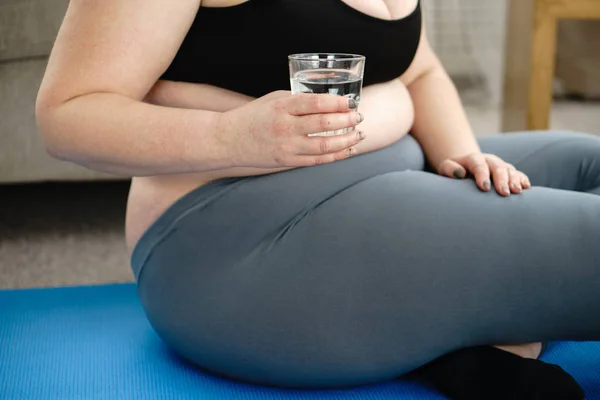 Donna in sovrappeso beve acqua, yoga a casa allenamento — Foto Stock