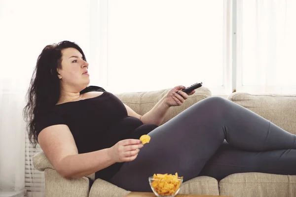 Kobieta z pilota od telewizora i Fast-food z nadwagą — Zdjęcie stockowe