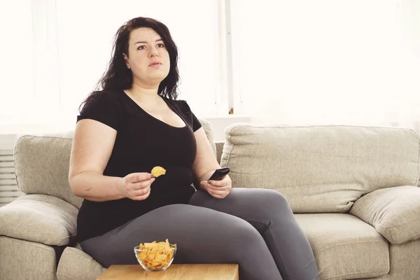 Надмірна вага жінки з телевізором віддаленою і нездоровою їжею — стокове фото