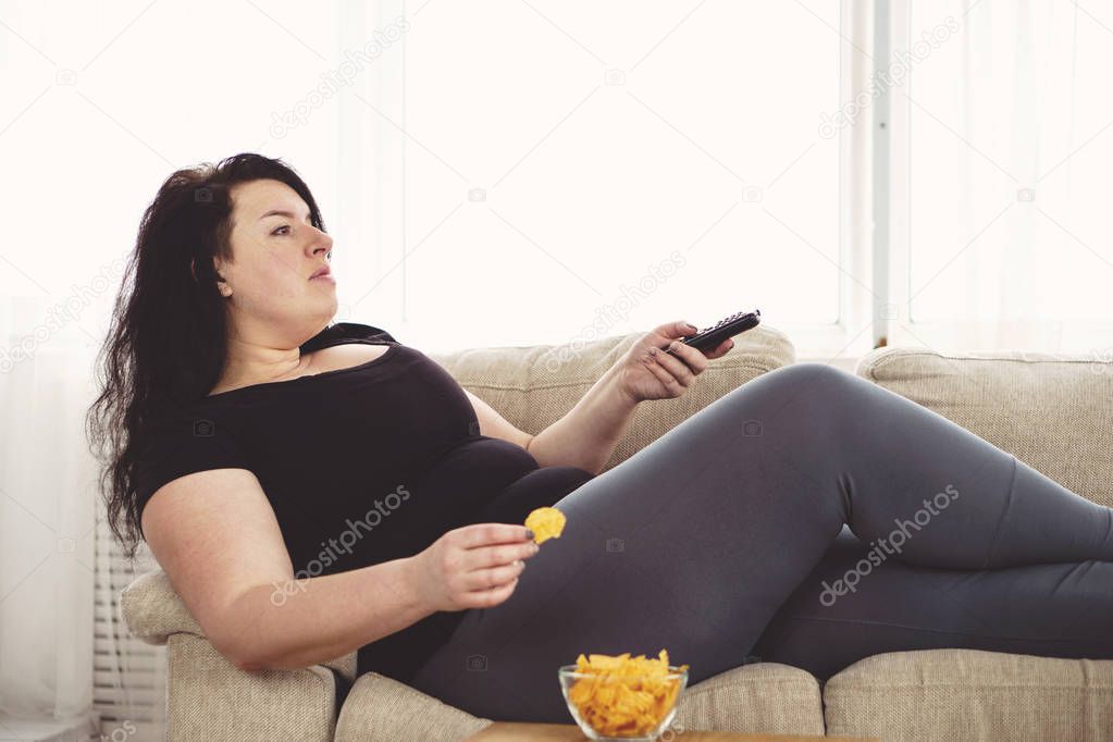 overweight woman with tv remote and junk food 