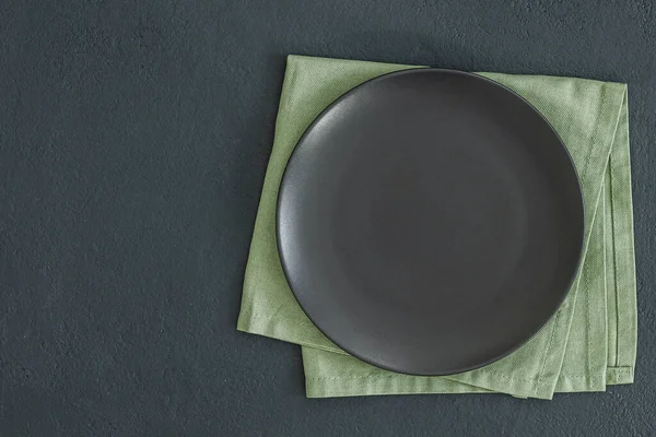 Empty black slate plate on dark stone table and napkin. Food background for menu, recipe. Table setting. Flatlay, top view. Mockup for restaurant dish