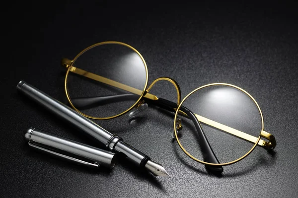 金色框架经典圆形眼镜和钢笔在黑色背景上 — 图库照片