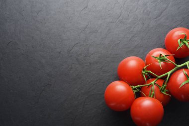 Red tomatoes on black slate with copy space