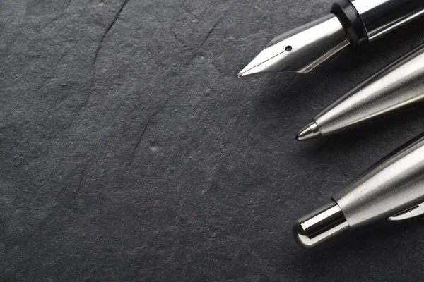 Metal ballpoint and fountain pen on black slate background — Stok fotoğraf