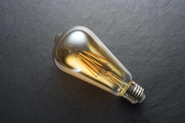 Transparent LED filament light bulb on black slate background. — Stock Image Transparent LED filament light bulb on black slate background. Stock Image