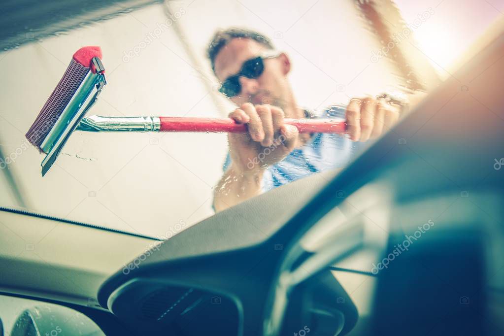 Caucasian Men in His 30s Cleaning His Car Windshield by Removing Water From the Glass.