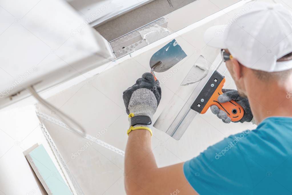 Building Drywall Ceiling Elements For LED Lighting. Caucasian Worker Patching Drywall.