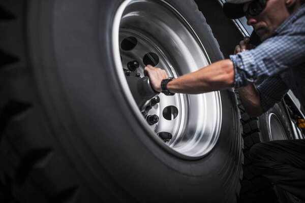 Caucasian Driver Checking Semi Truck Wheels. Transportation Industry.