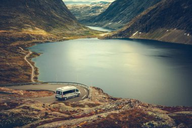 RV Camper Scenic Road Trip. Raw Norwegian Landscape and the Camper Van Recreational Vehicle on the Winding Mountain Road near Famous Village of Geiranger. clipart