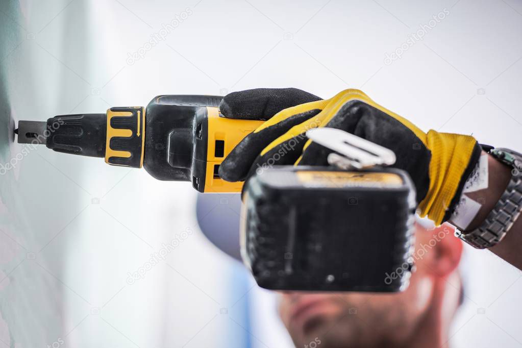 Drywall Installation Project. Caucasian Construction Worker with Drill Driver Closeup Photo.