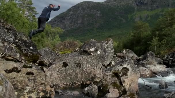 野外活動を楽しむ白人男性 川の岩の間にジャンプします スローモーション映像 — ストック動画