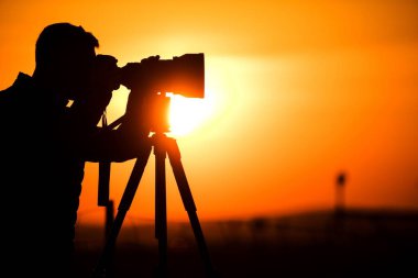 Gün batımı sırasında bir Tripod üzerinde kamera ile fotoğraf hobisi silüeti.