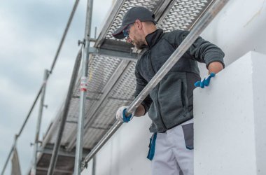 İskele üzerinden yalıtım yapı. Beyaz inşaat işçisi elinde yalıtım malzemesi ile.