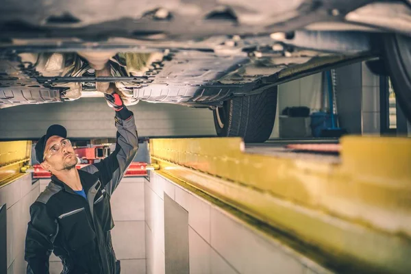 Vehicle Diagnostic Station. Caucasian Auto Service Worker Checking Car Under Carriage Looking For Potential Issues.