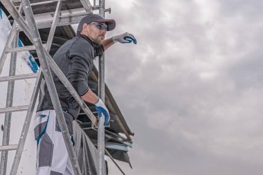 İnşaat Sanayi tema. Beyaz inşaat işçisi onun 30s Metal iskele üzerinde. 