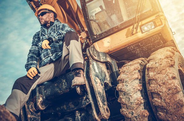 Caucasian Excavator Operator Sitting on His Excavator. Heavy Duty Ground Working Machinery. Construction Industry.