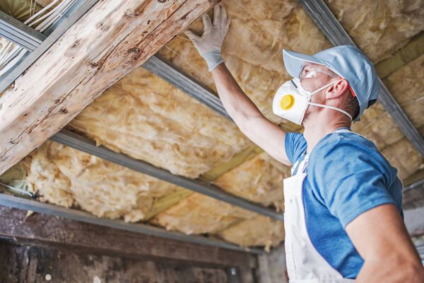 Old Roof Insulation. Caucasian Construction Worker in His 30s Inspecting Aged Roof and Mineral Wool Insulator.