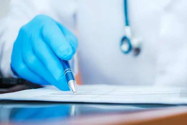 Arzt Mit Blauen Handschuhen Unterschreibt Notwendige Unterlagen — Stockfoto