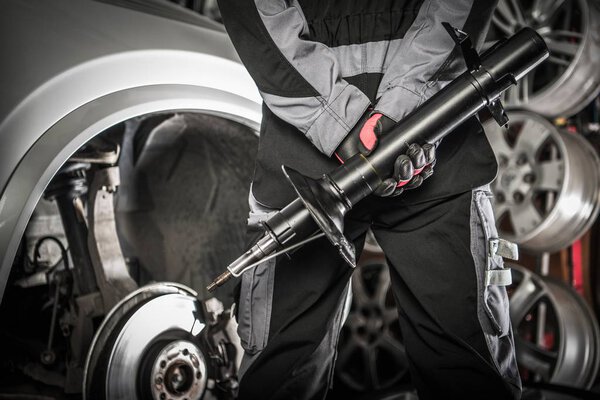 Automotive Concept. Car Mechanic with Shock Absorber Hydraulic Device in Hands Preparing For Necessary Absorbers Change.