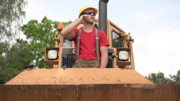 Operador de Equipo Pesado Caucásico Permaneciendo en Bulldozer y Hablando por Teléfono . — Vídeo de stock