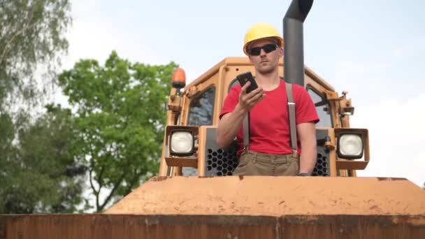 Bulldozer operator Making telefon podczas pobytu na jego maszynie. Budownictwie. — Wideo stockowe