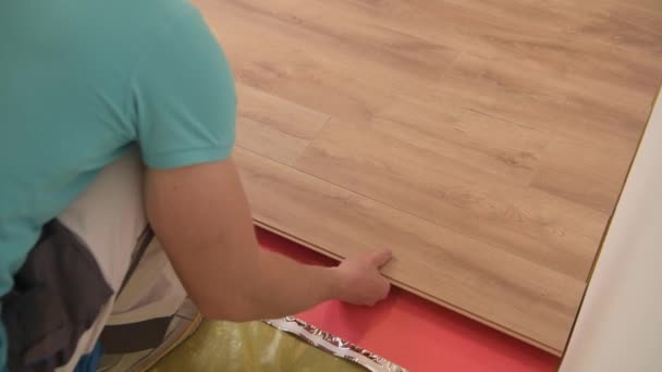 フロアパネルインストーラ。30代の白人リモデラーワーカーが新しい木製の床を設置. — ストック動画