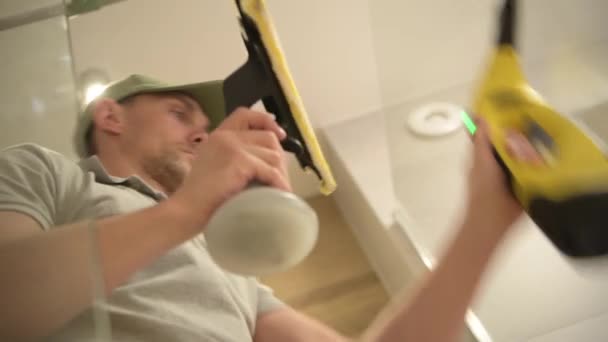 Mannen in zijn 30s schoonmaken douchecabine in zijn badkamer — Stockvideo