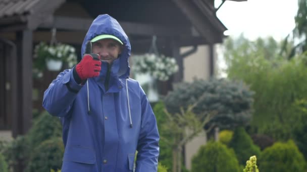 Trabalhador de jardim caucasiano em capa de casaco molhado mostrando polegar para cima . — Vídeo de Stock