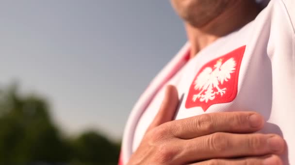 Poolse voetbal fan trots om deel uit te maken van de wedstrijd houden zijn hand op het hart in de buurt van Pools nationaal symbool. — Stockvideo